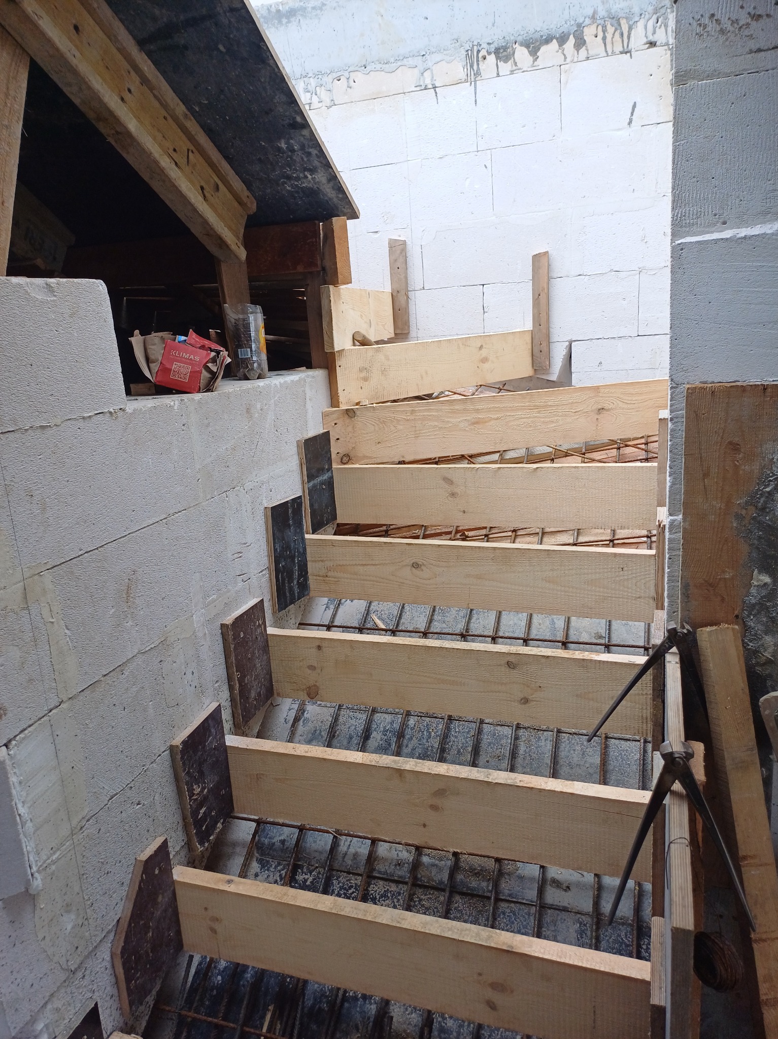 Konstrukcja szalunku drewnianego ze stalą zbrojeniową przygotowana pod wylanie betonowych schodów w budynku z białych bloczków.