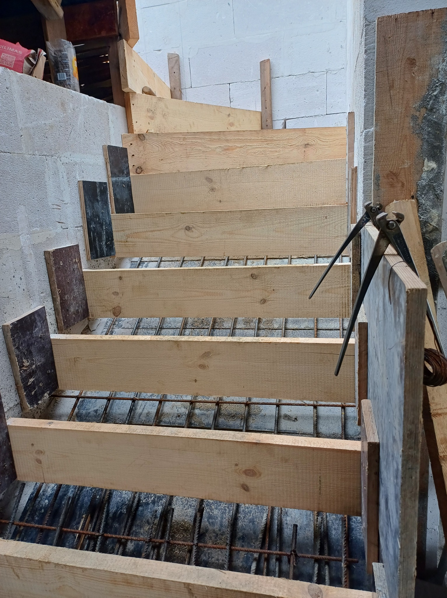 Konstrukcja szalunku drewnianego pod schody żelbetowe z widocznym zbrojeniem i narzędziami do wiązania drutu.