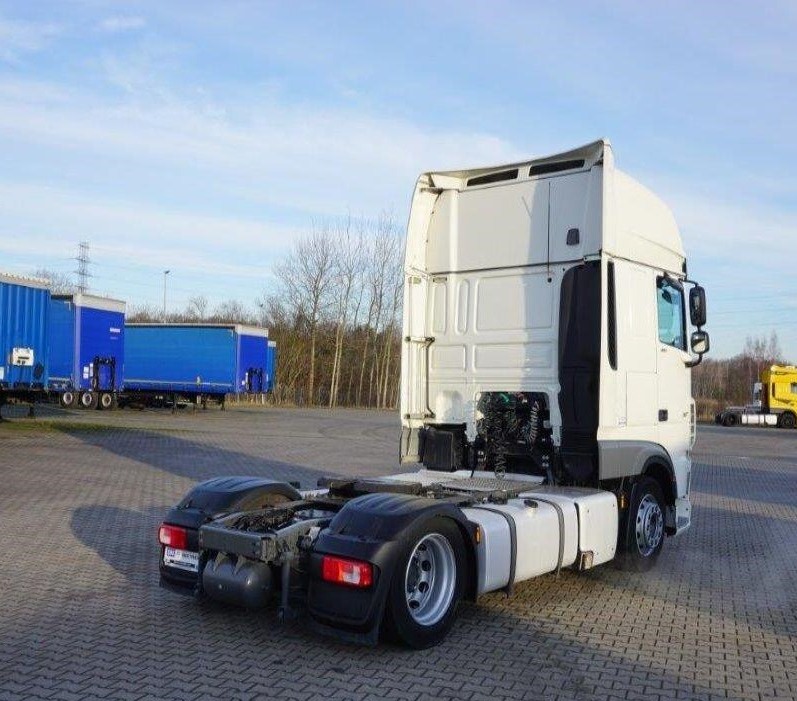 Biały ciągnik siodłowy DAF bez naczepy, widok z tyłu na placu manewrowym, w tle błękitne kontenery i żółty pojazd.