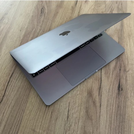 Otwarty srebrny laptop z logo Apple na drewnianym blacie, widoczne klawisze i touchpad.