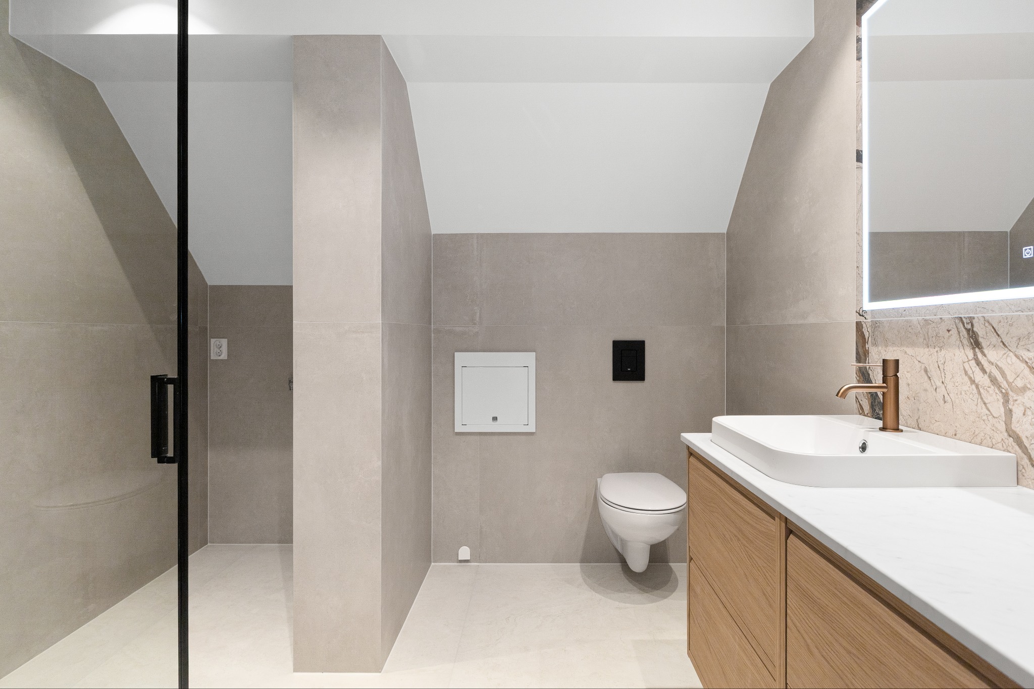 Nowoczesna łazienka na poddaszu z kabiną prysznicową, umywalką nablatową i WC. Jasne płytki, drewniane szafki pod umywalką i oświetlone lustro.