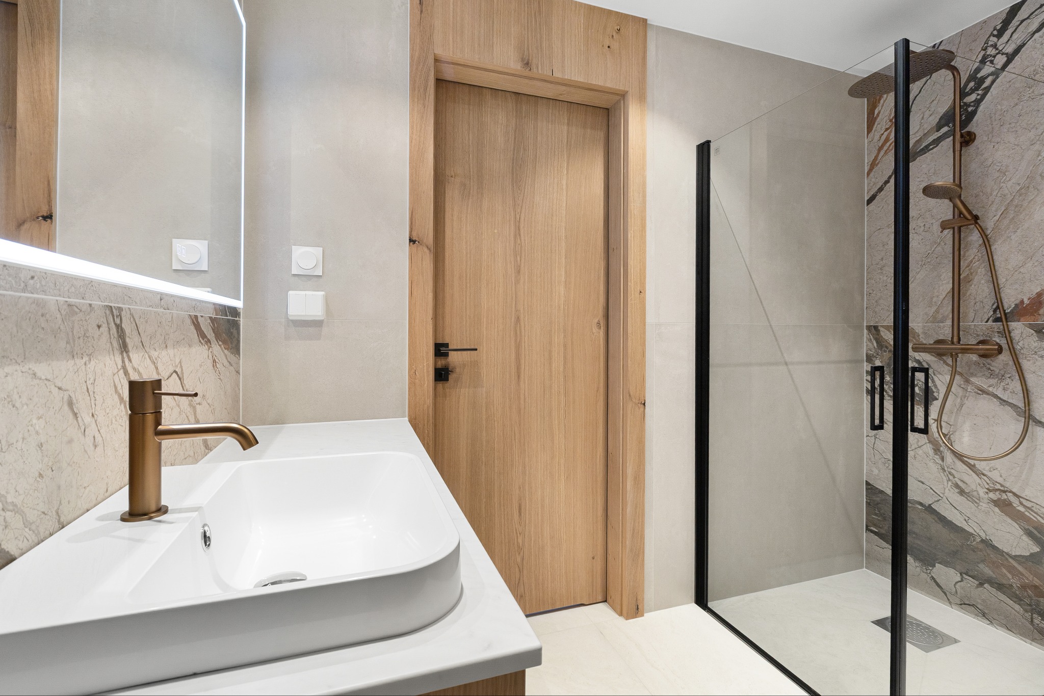 Nowoczesna łazienka z drewnianymi drzwiami, umywalką nablatową z miedzianą armaturą i kabiną prysznicową z czarnymi profilami. Minimalistyczny design.