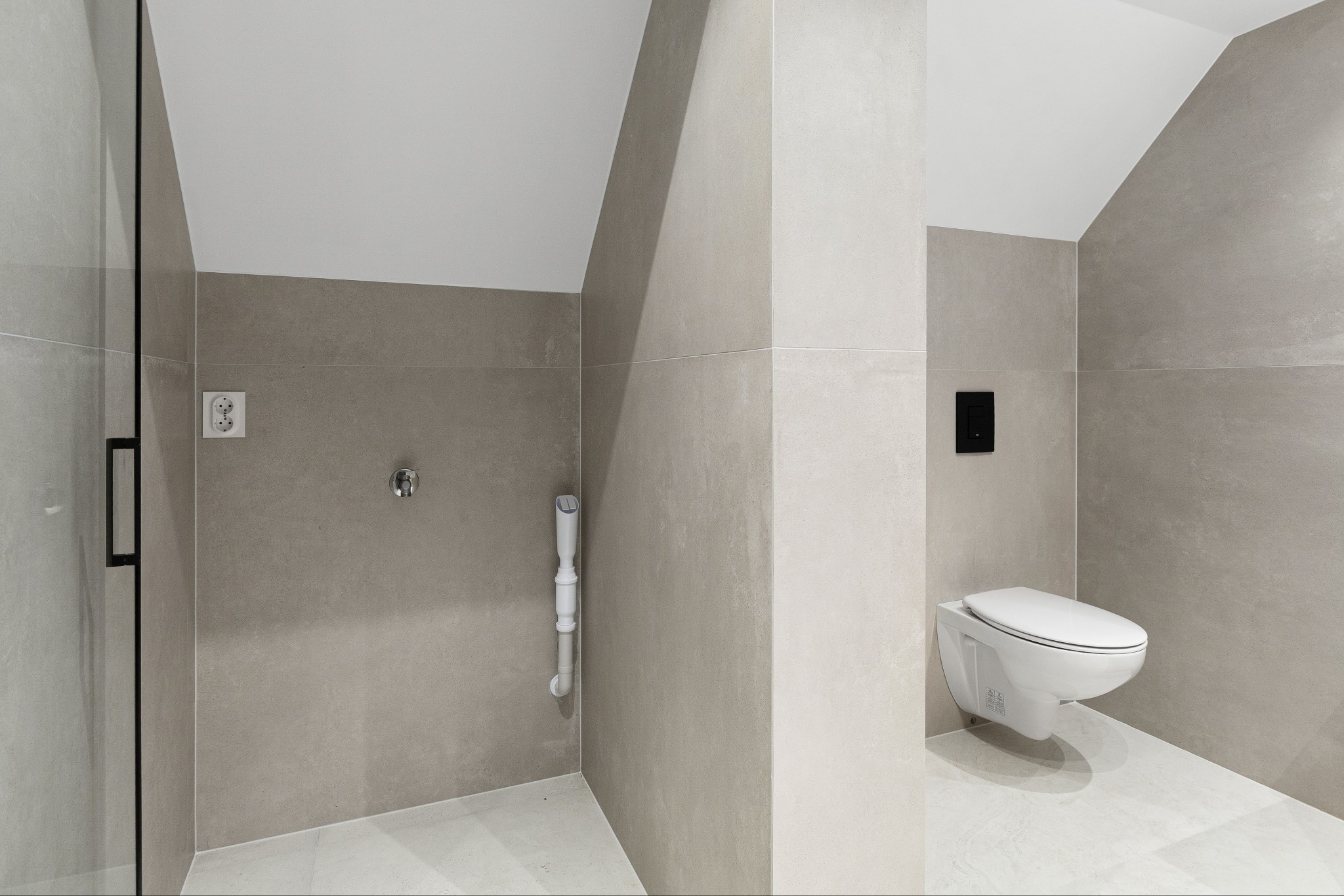 Nowoczesna łazienka w odcieniach szarości z podwieszaną toaletą, szklaną kabiną prysznicową i subtelnym oświetleniem, ukazująca minimalistyczny design i funkcjonalność.