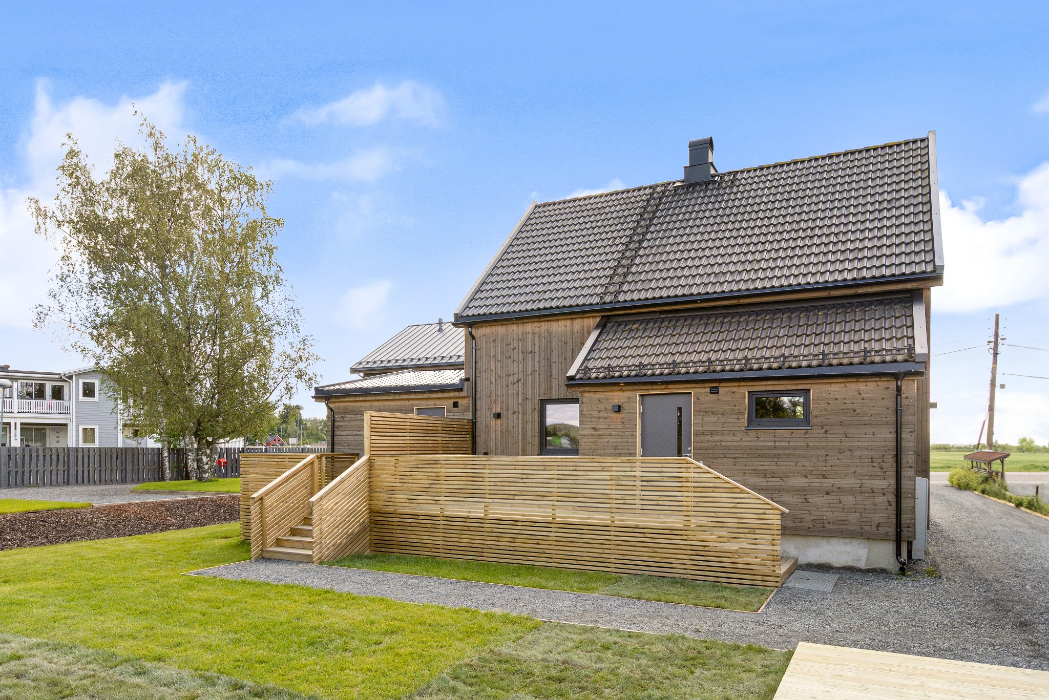 Nowoczesny dom szkieletowy z drewnianą elewacją i tarasem z jasnego drewna, widok z zewnątrz w słoneczny dzień. Minimalistyczny design i naturalne materiały.