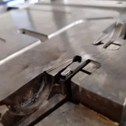 Metalowa forma z precyzyjnie obrobionymi wgłębieniami i rowkami, widoczne ślady obróbki skrawaniem, detale mocowania, ostre krawędzie i powierzchnie