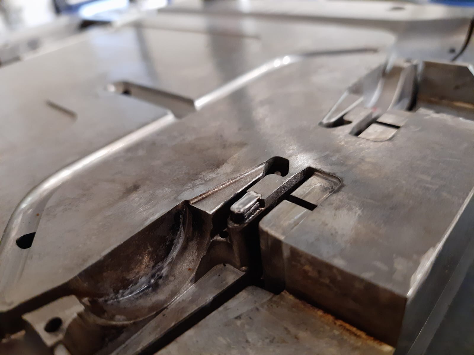 Metalowa forma z precyzyjnie obrobionymi wgłębieniami i rowkami, widoczne ślady obróbki skrawaniem, detale mocowania, ostre krawędzie i powierzchnie