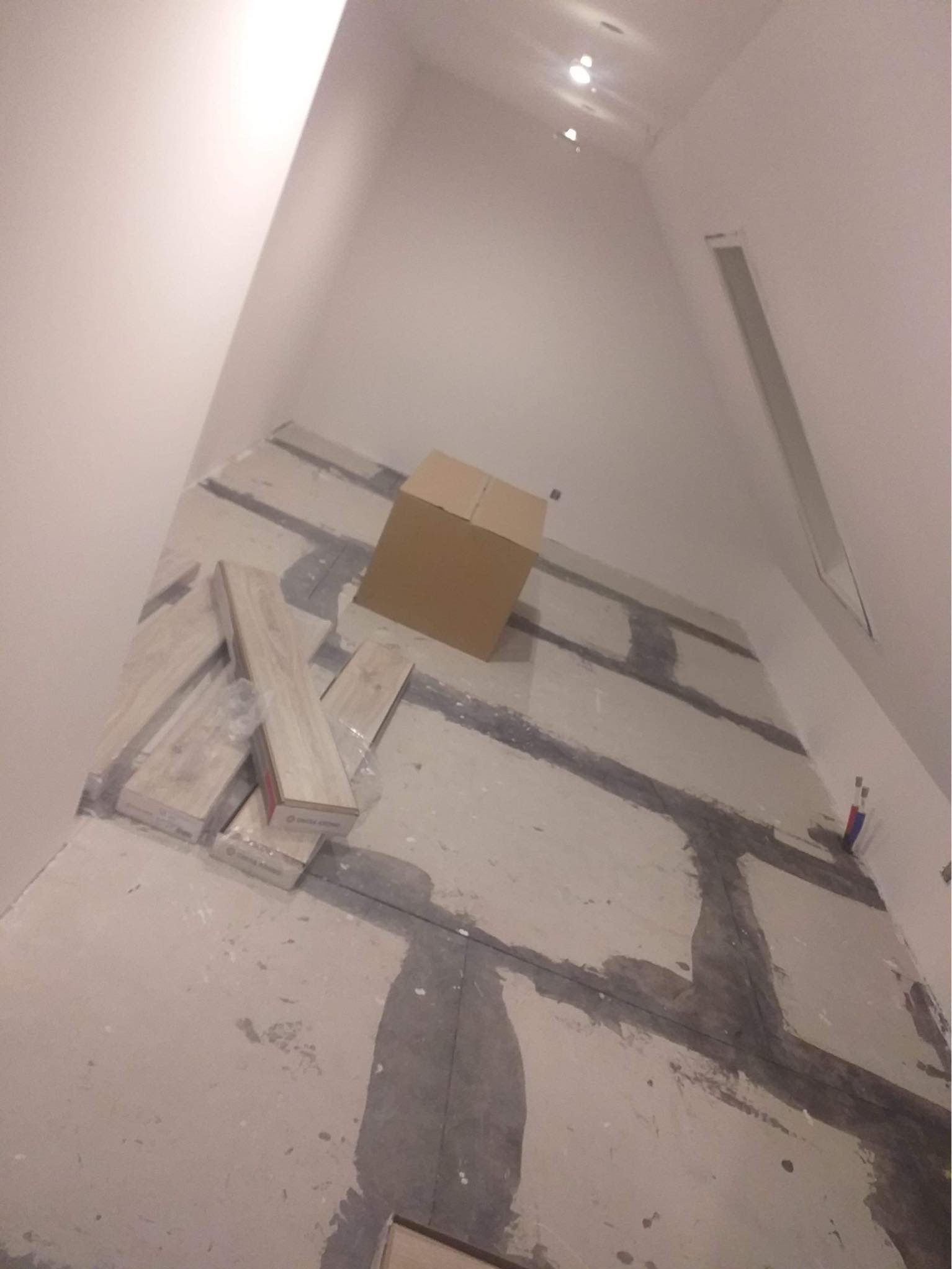 Przygotowanie do malowania: surowy stan podłogi z zaznaczonymi liniami, karton i paczki paneli podłogowych w rogu pomieszczenia.