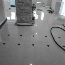 Mrówki polskie przedsiębiorstwo budowlane - Błyszcząca, jasna podłoga z płytek w romby, kolumna wykończona kamieniem dekoracyjnym, widoczne narzędzia i elementy wyposażenia, wnętrze w trakcie prac wykończeniowych.