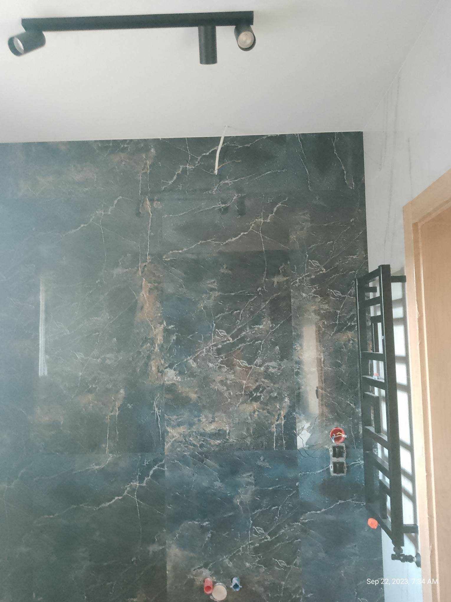 Ciemnozielona ściana z płytek imitujących marmur w łazience w trakcie prac wykończeniowych, widoczne puszki elektryczne bez osprzętu i grzejnik drabinkowy.