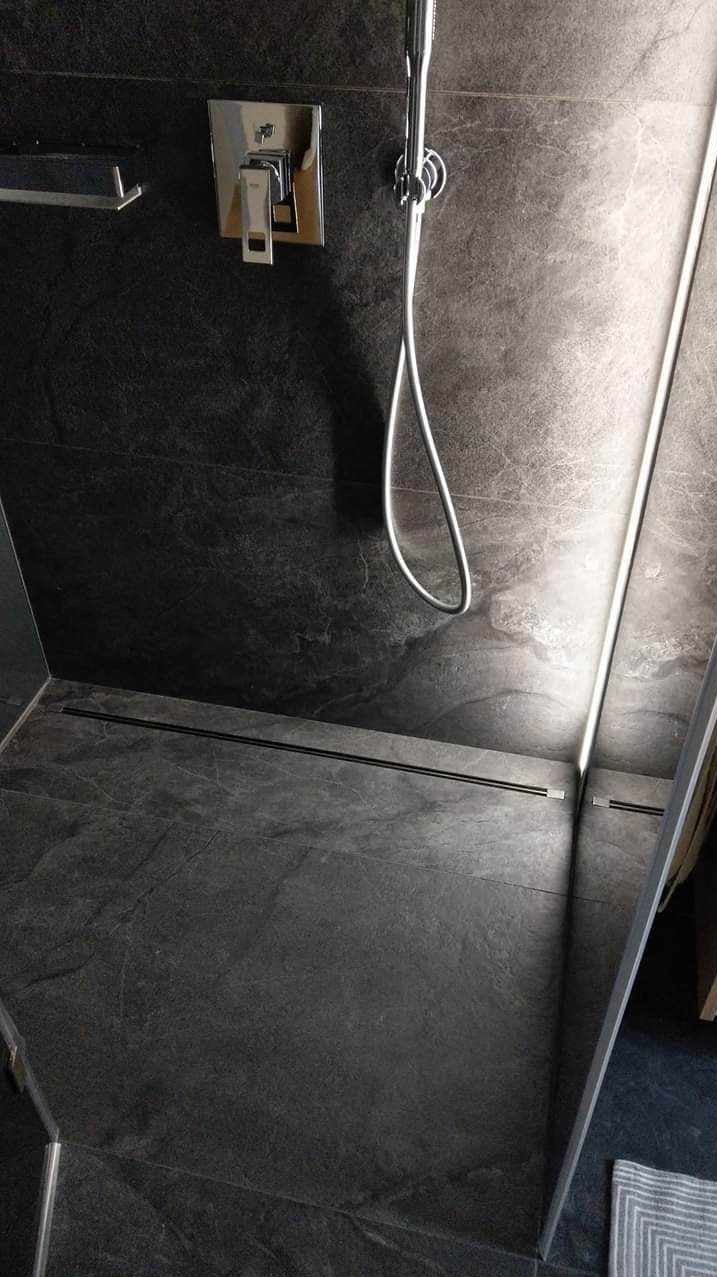 Nowoczesna kabina prysznicowa z ciemnoszarą, kamienną okładziną ścian i podłogi, wyposażona w chromowaną armaturę i odpływ liniowy.