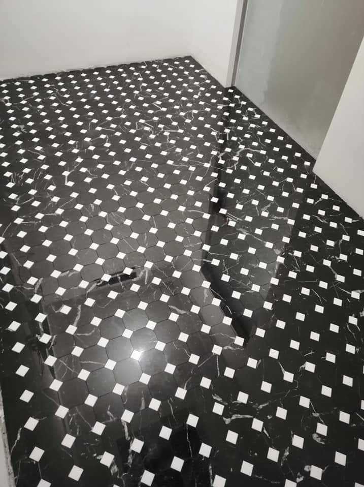 Ułożona pod kątem podłoga z czarnych, marmurkowych płytek w kształcie ośmiokątów z białymi kwadratowymi wstawkami, tworząca wzór szachownicy.