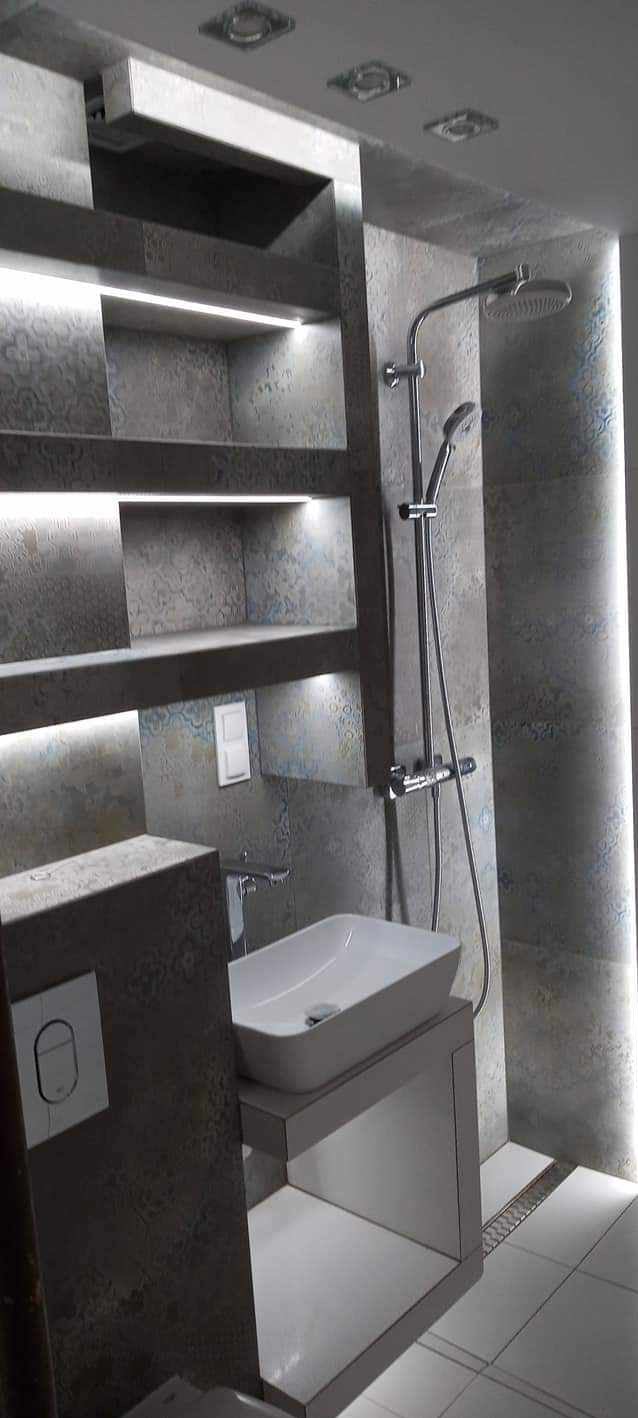 Nowoczesna łazienka z szarymi płytkami o wzorzystej fakturze, podświetlane półki w ścianie, biała umywalka nablatowa i chromowana bateria, deszczownica z regulacją wysokości, odpływ liniowy...