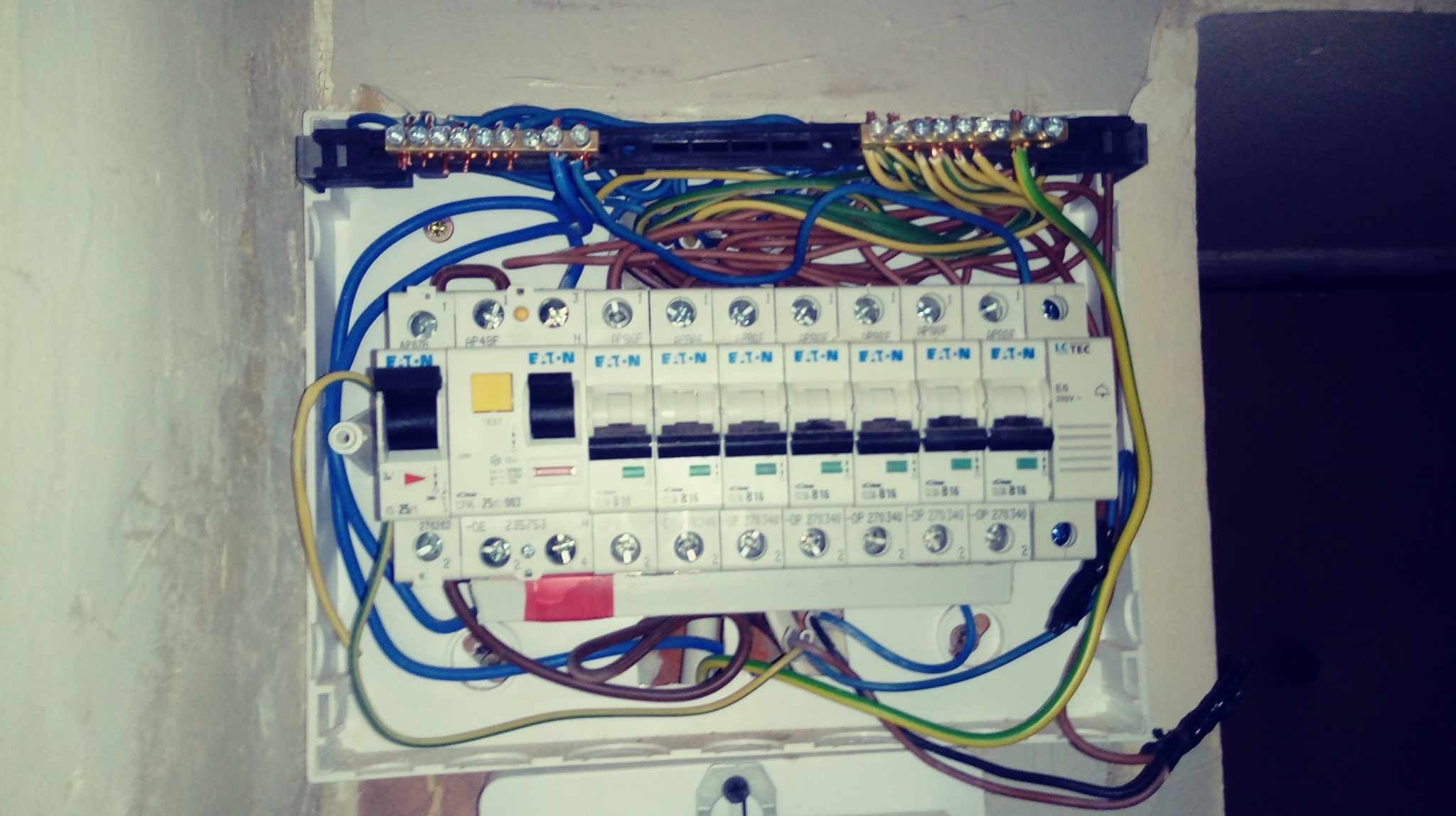 Otwarta skrzynka bezpiecznikowa z widocznymi bezpiecznikami marki EATON, okablowaniem i listwami zaciskowymi, zamontowana na ścianie.