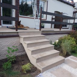 pk-bud - Zewnętrzne schody z płytek prowadzące na taras z drewnianą balustradą, na którym leży pies rasy owczarek niemiecki, obok drabina oparta o ścianę budynku.