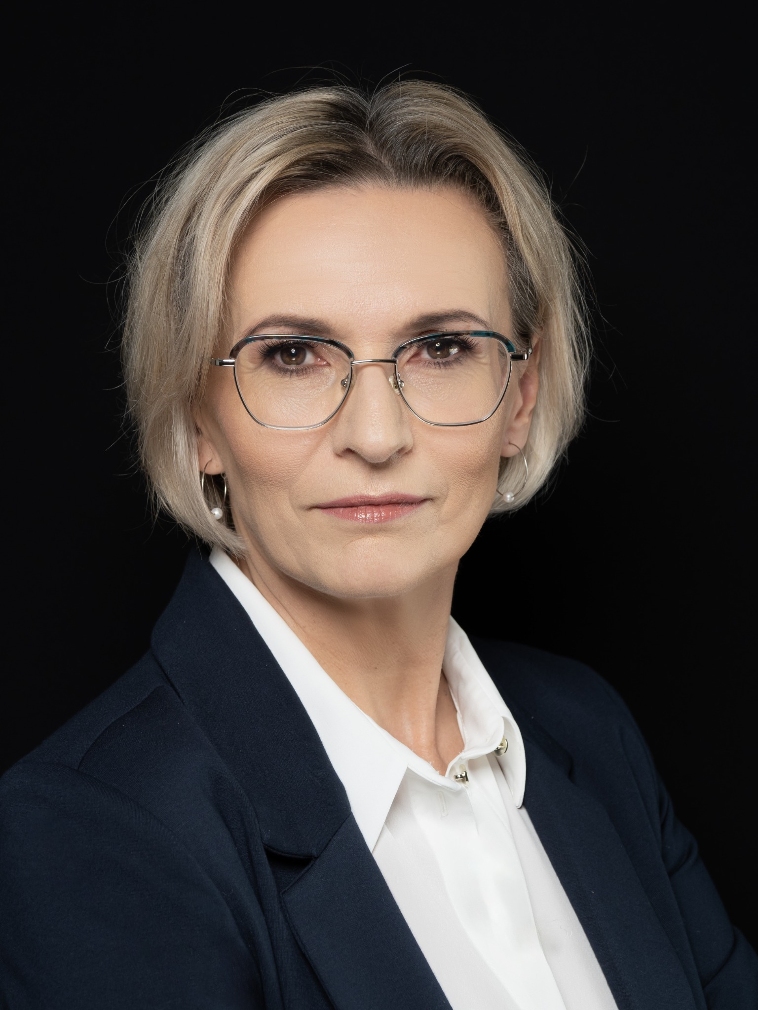 Portret kobiety w okularach, białej koszuli i granatowej marynarce na czarnym tle, wykonany w studio w Warszawie.