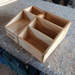 Maciej Kukuła - Drewniany organizer z przegródkami i szufladą, wykonany z jasnego drewna, leżący na stole warsztatowym pokrytym wiórami.