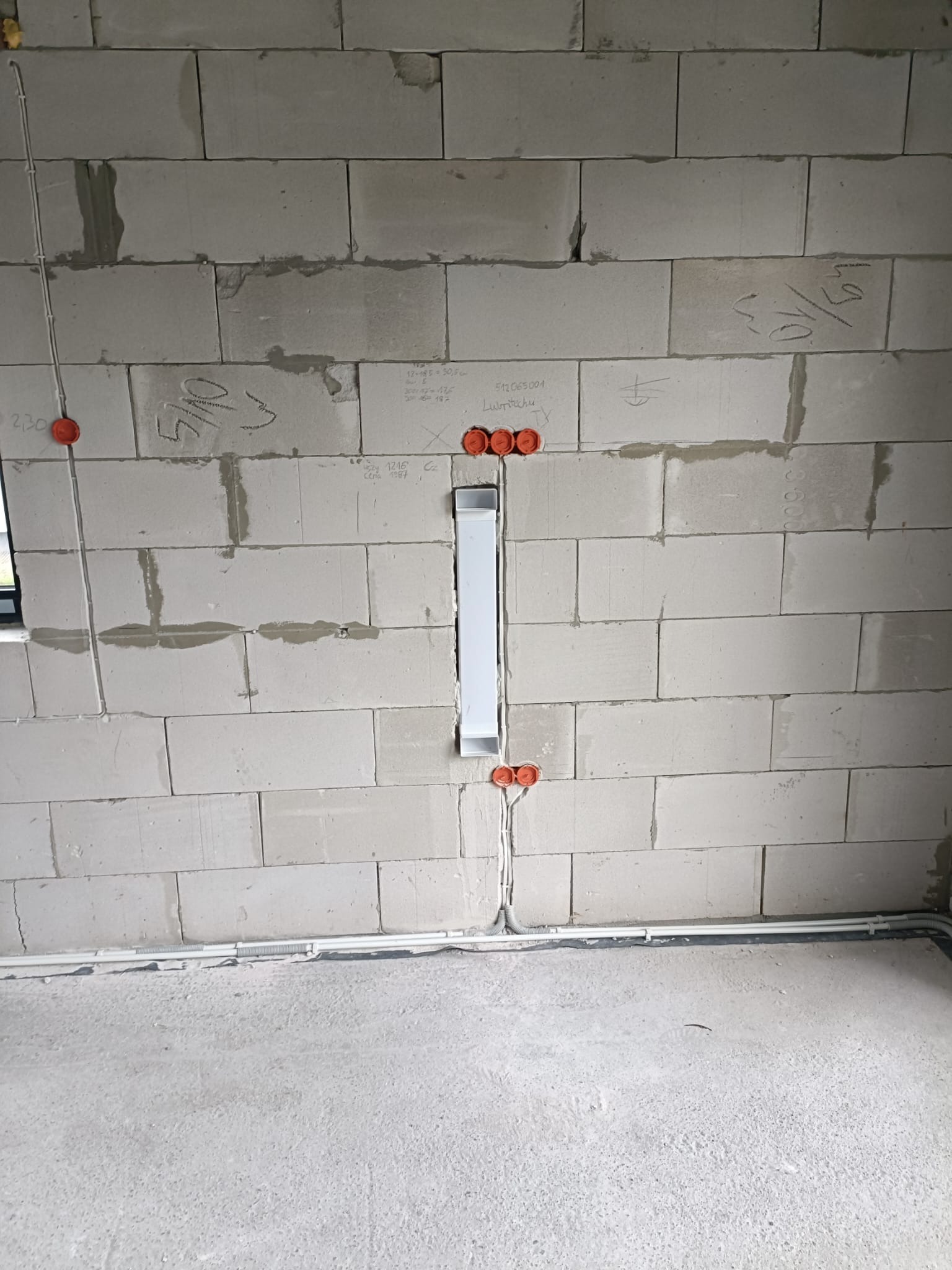 Instalacja elektryczna w surowym wnętrzu: kable w peszlach, puszki podtynkowe w ścianie z betonu komórkowego. Widoczne oznaczenia na ścianie.