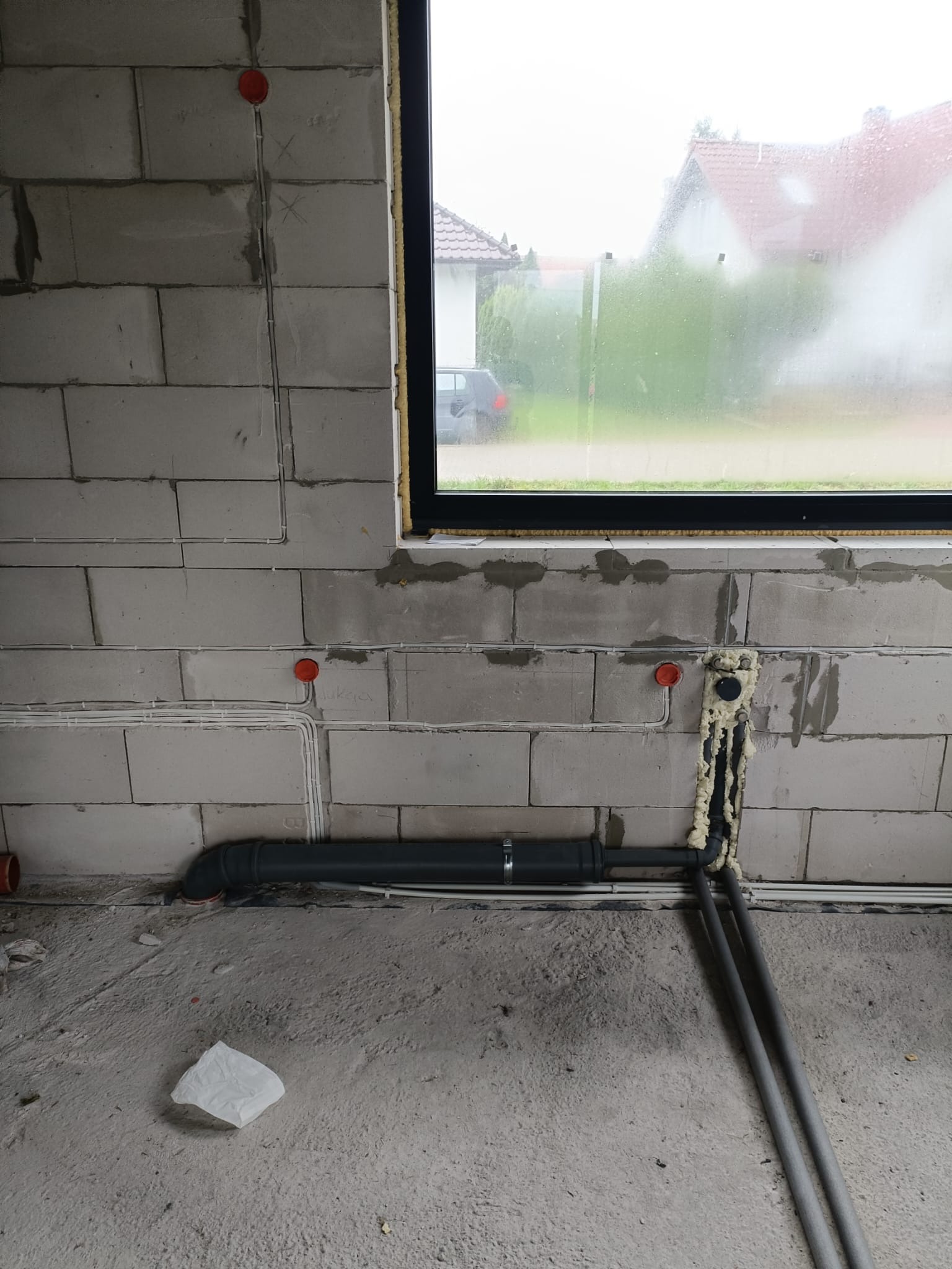 Surowy stan: instalacja wodno-kanalizacyjna przy oknie w ścianie z betonu komórkowego. Widoczne przewody elektryczne w bruzdach i pianka montażowa.