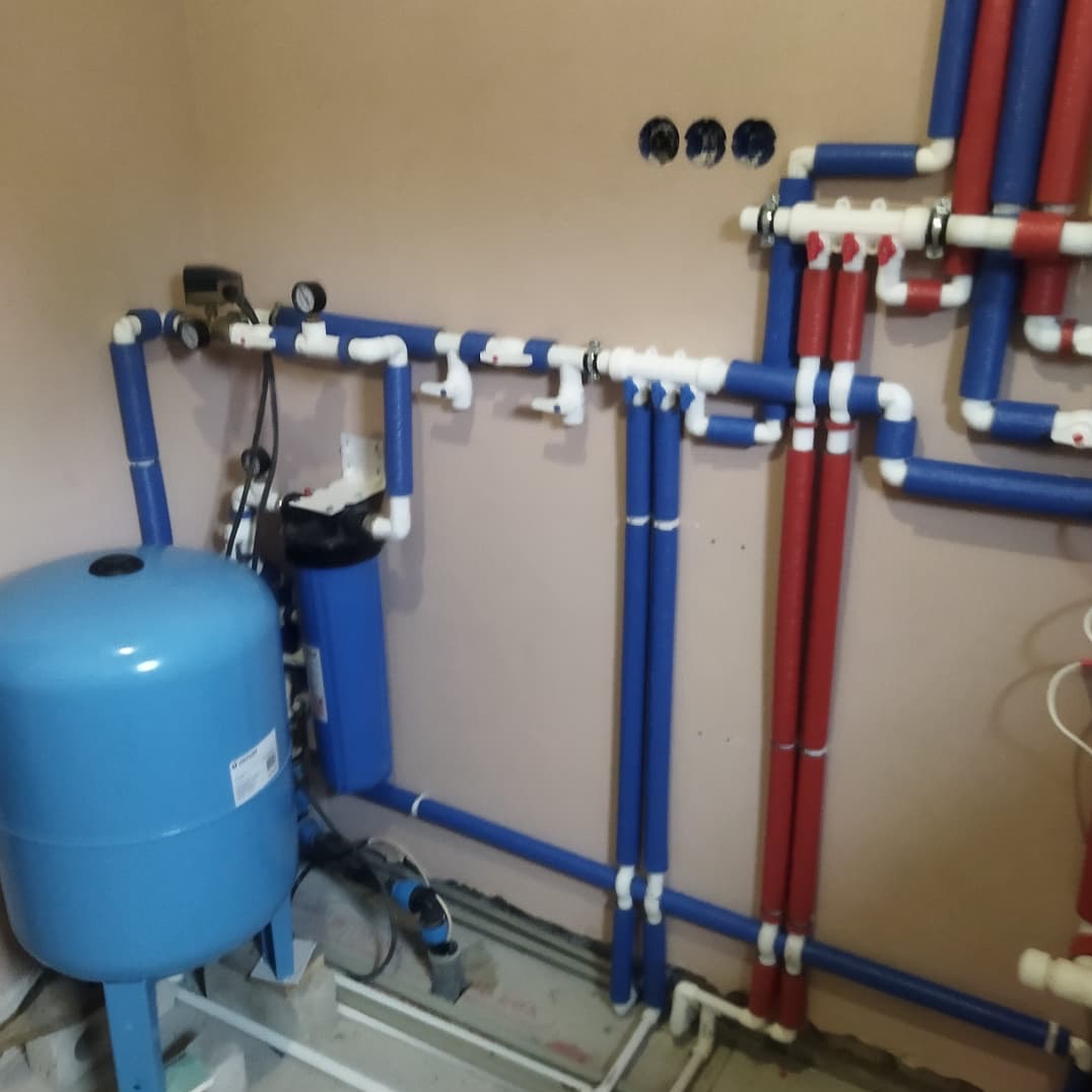 Instalacja wodna z niebieskim zbiornikiem ciśnieniowym, filtrem wody i rurami w izolacji, widoczne manometry i zawory.
