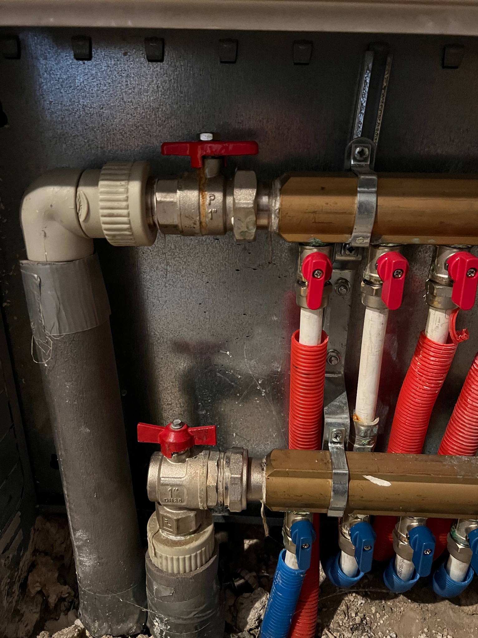 Rozdzielacz ogrzewania podłogowego z zaworami termostatycznymi, rurami w peszlach i przyłączami, widoczne detale instalacji w metalowej szafce.