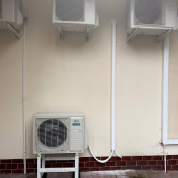 KLIMAZEN SPÓŁKA Z OGRANICZONĄ ODPOWIEDZIALNOŚCIĄ - Cztery jednostki klimatyzacyjne Fujitsu Airstage zamontowane na ścianie budynku, z widocznymi rurami instalacyjnymi i wspornikami, na zewnątrz budynku.