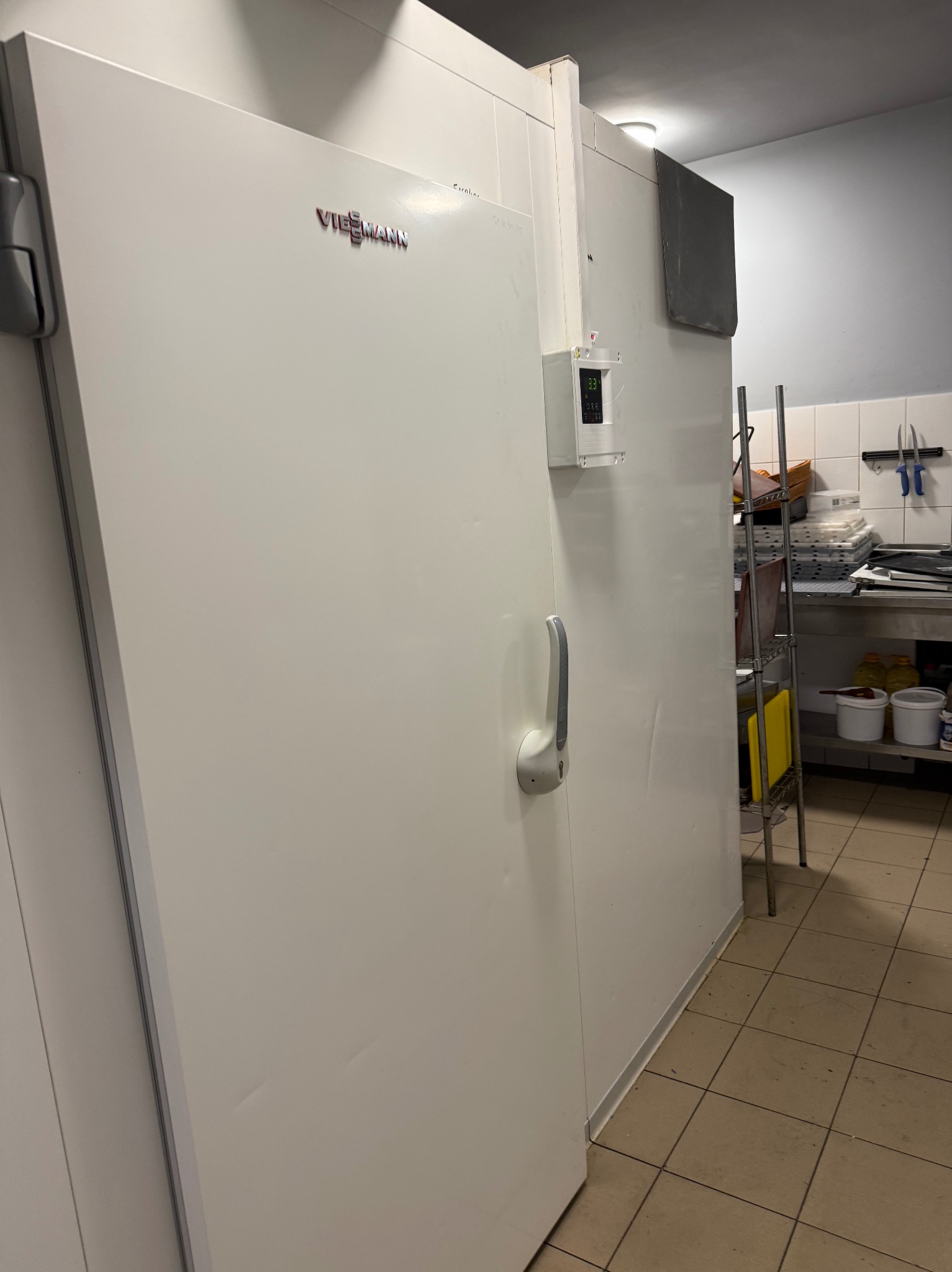 Biała chłodnia Viessmann z panelem sterowania w pomieszczeniu gastronomicznym, widoczny fragment wyposażenia kuchni i podłoga z płytek.