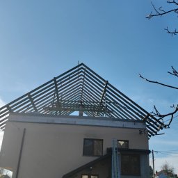 Usługi budowlane WenDach - Dom jednorodzinny w trakcie budowy dachu, widoczna drewniana konstrukcja więźby dachowej na tle błękitnego nieba, z fragmentem drzewa z prawej strony
