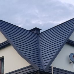 Usługi budowlane WenDach - Ciemna dachówka modułowa na skośnym dachu domu jednorodzinnego. Widoczny komin i orynnowanie. Częściowo ocieplona ściana szczytowa. Pochmurne niebo w tle.