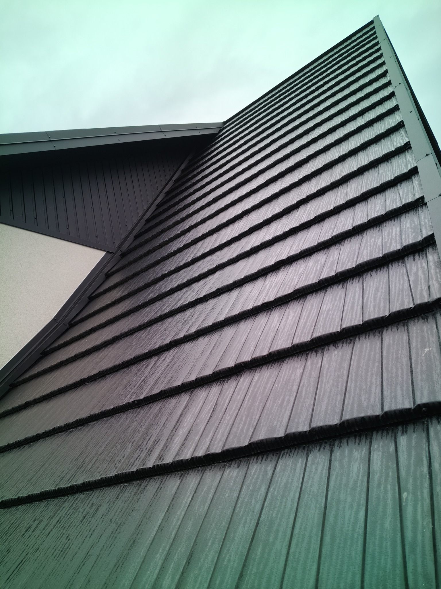 Szary dach z blachy trapezowej, widok z dołu pod kątem, fragment ściany budynku. Nowoczesne pokrycie dachu w zbliżeniu.