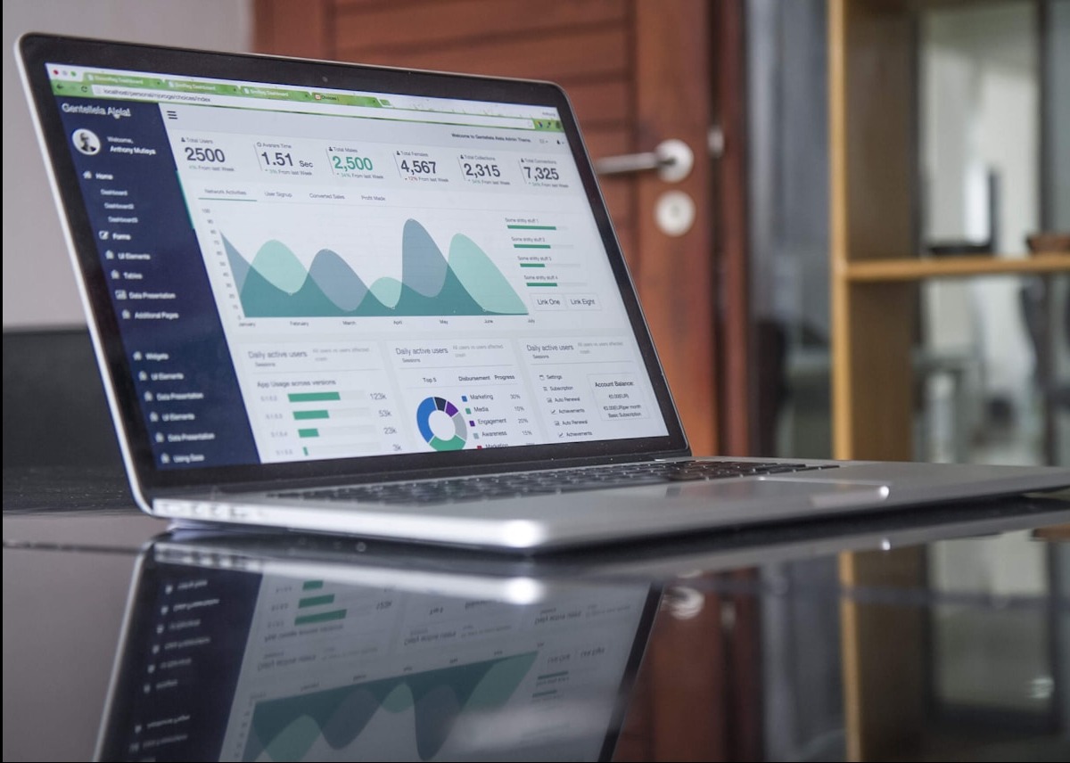 Laptop wyświetlający dashboard z wykresami i danymi analitycznymi na błyszczącej powierzchni biurka, widoczne odbicie ekranu.