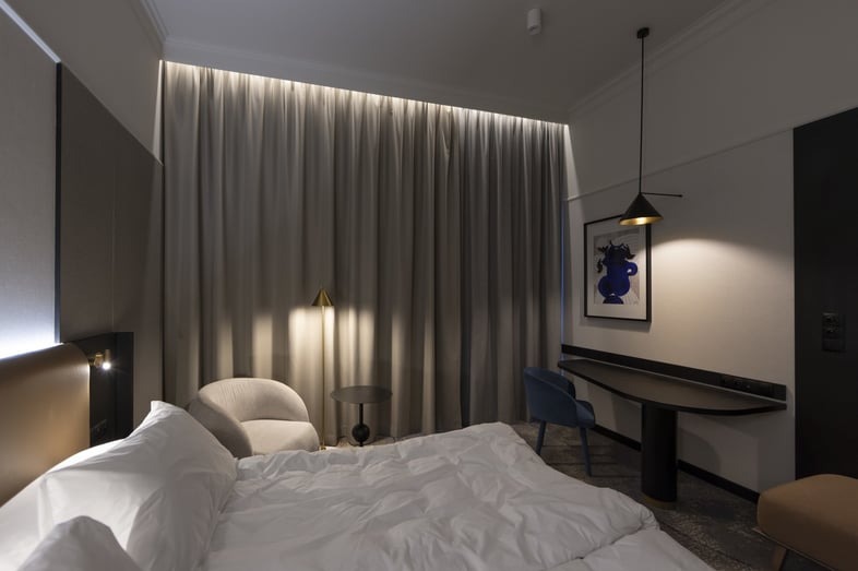 Nowoczesna sypialnia z podświetlanymi zasłonami, lampą wiszącą nad biurkiem i kinkietem nad wezgłowiem łóżka.