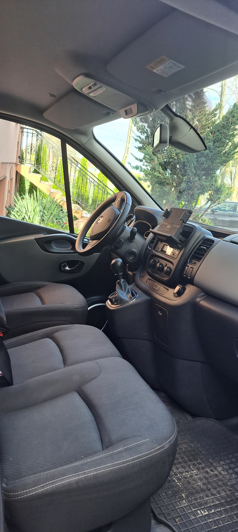 Wnętrze busa: kierownica, deska rozdzielcza z uchwytem na telefon, dźwignia zmiany biegów i fotele z ciemną tapicerką. Widok z perspektywy pasażera.