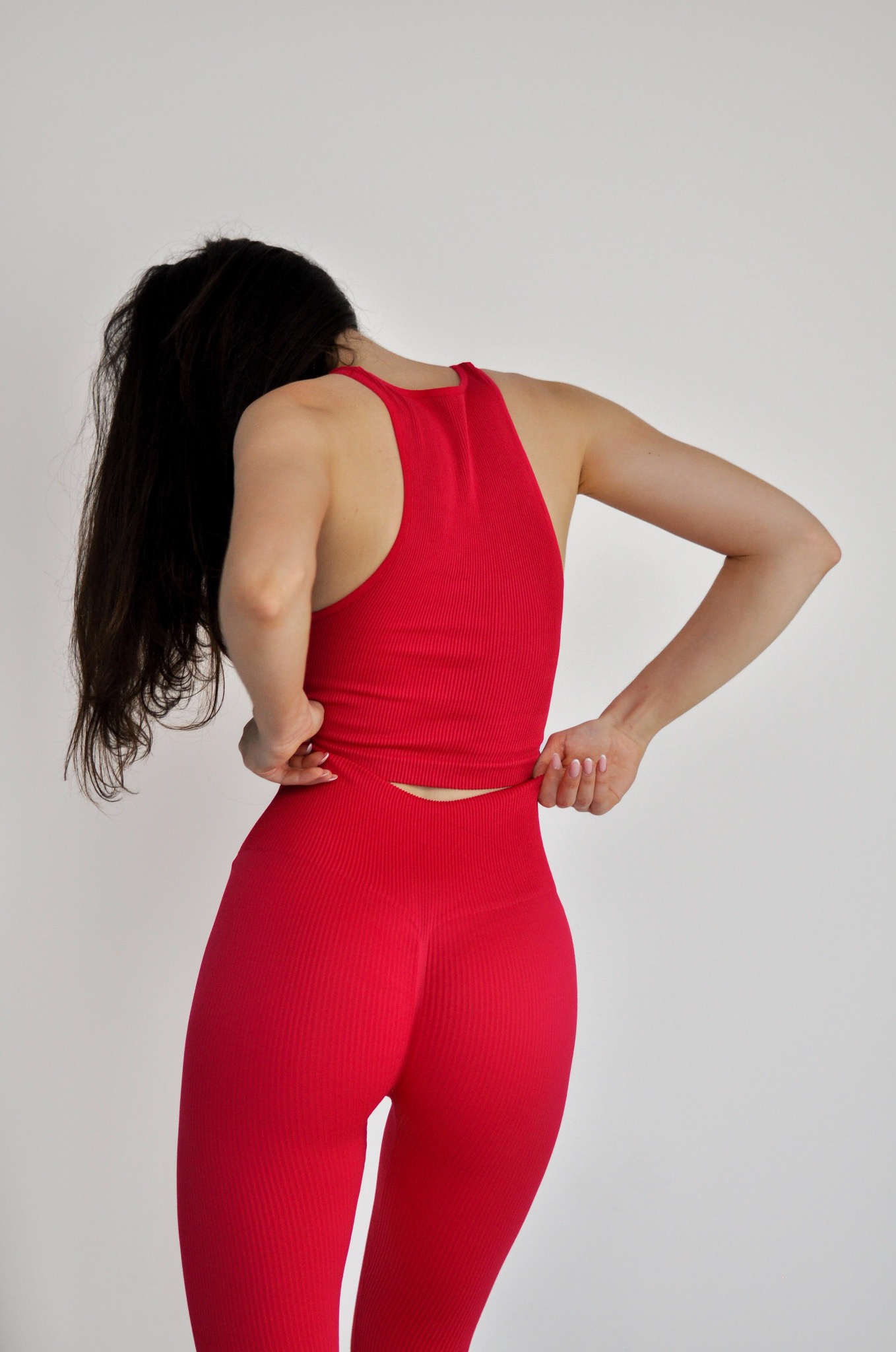 Kobieta w dopasowanym, czerwonym komplecie sportowym z prążkowanej dzianiny, tyłem do obiektywu, poprawia górę stroju.