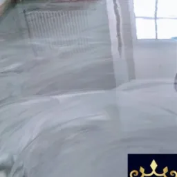 Błyszcząca, szara podłoga z efektem marmuru, widoczny grzejnik i okno w tle, w prawym dolnym rogu logo firmy M&M Epoxy Design.