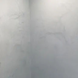 Ściana w rogu pomieszczenia pokryta szarą, dekoracyjną powłoką z subtelnymi, jaśniejszymi smugami i delikatnym połyskiem.