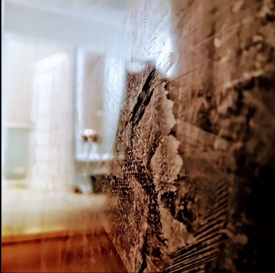 Szczegółowe zbliżenie na ścianę z efektem dekoracyjnym, prawdopodobnie w trakcie nakładania, z rozmytym tłem łazienki.