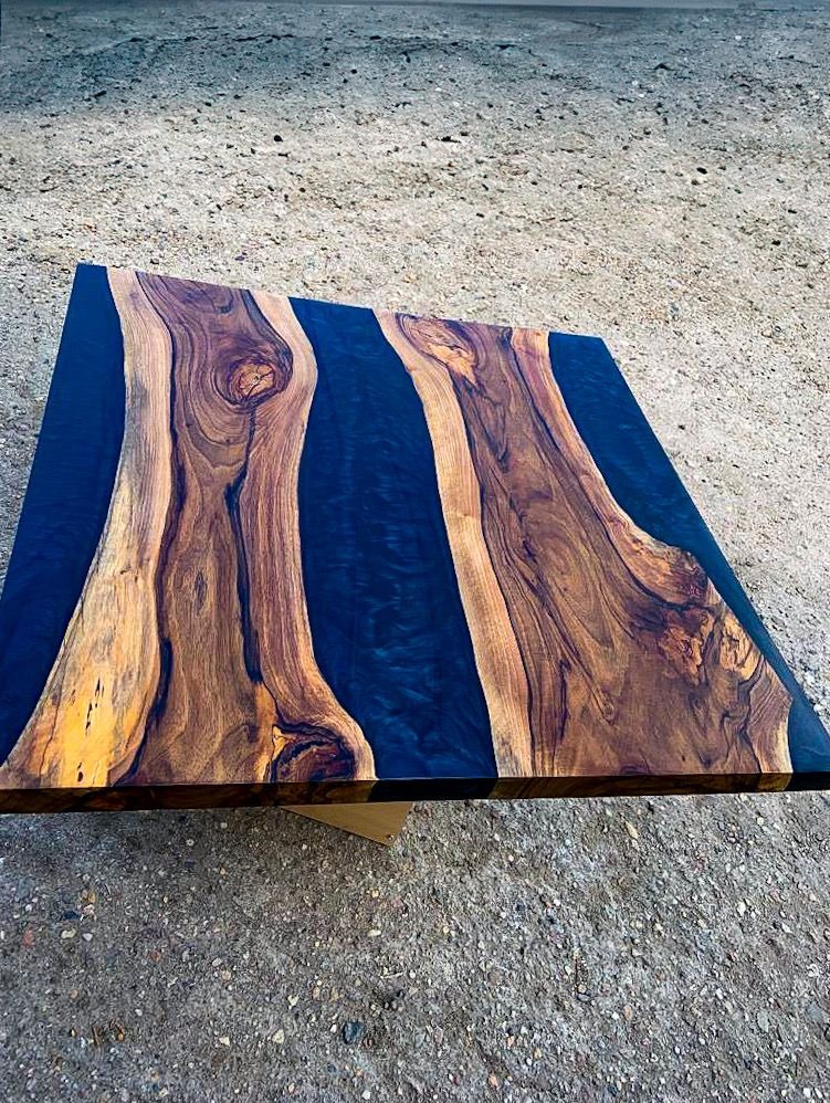 Stół z blatem z drewna z żywicą w kolorze głębokiego granatu, ukazujący naturalne słoje drewna, ustawiony na szarym, betonowym podłożu.