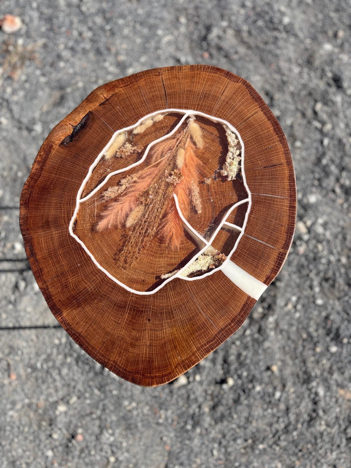 Drewniany stolik kawowy z żywicą epoksydową, w której zatopione są suszone kwiaty i trawy, całość na tle szarego żwiru.