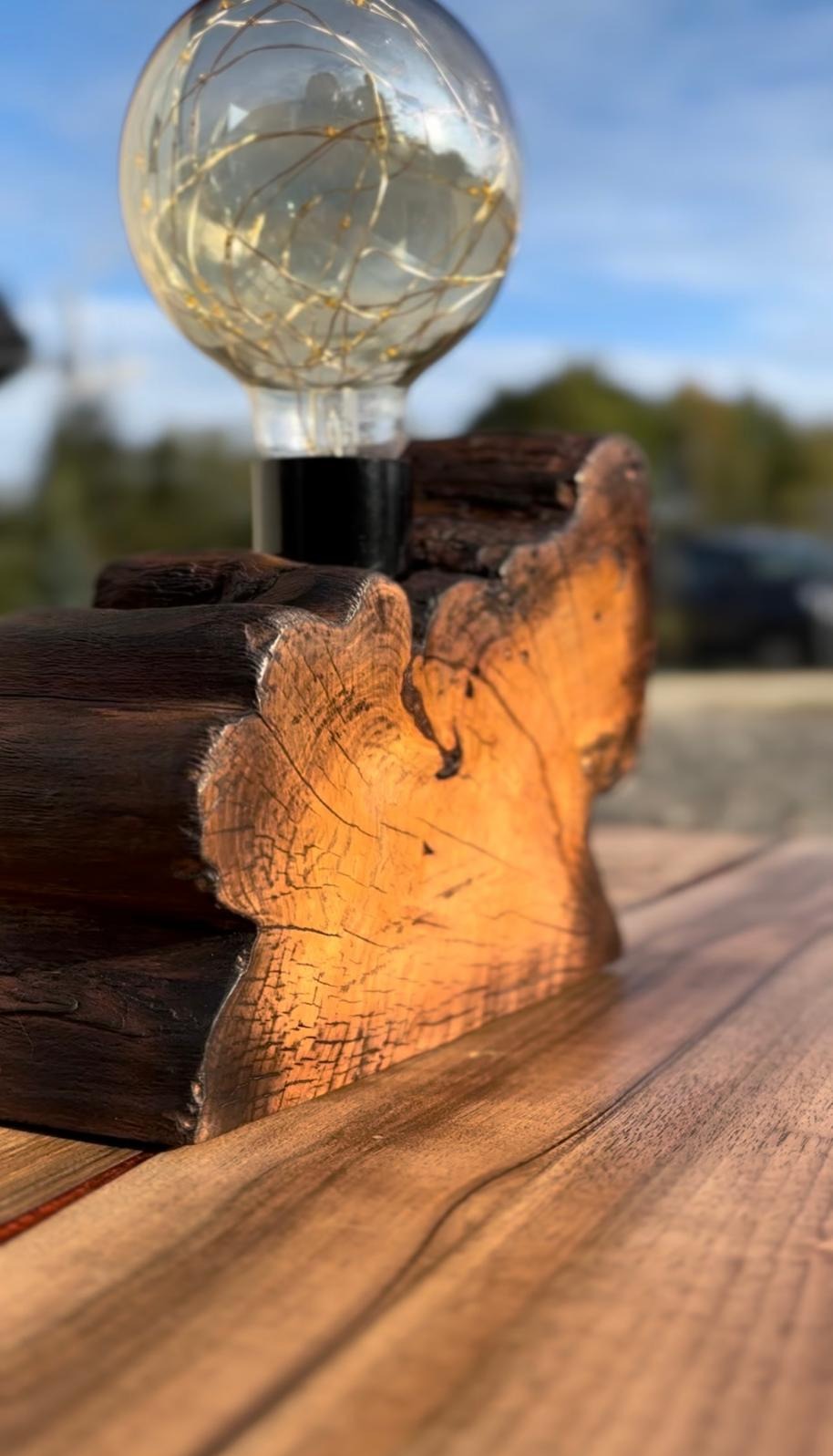 Lampa dekoracyjna z żarówką Edison i podstawą z surowego drewna na blacie drewnianym.