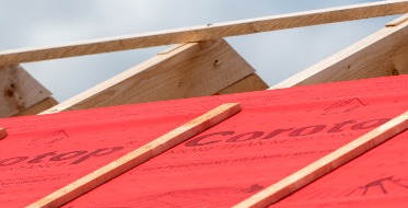 Czerwona membrana dachowa Corotop ułożona na drewnianej konstrukcji dachu w Radomiu, widok z dołu pod kątem, niebo w tle.