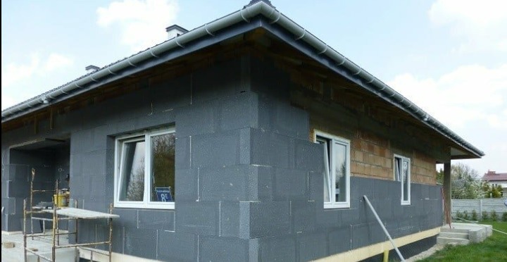Dom w trakcie ocieplania styropianem grafitowym, widoczne fragmenty muru i rusztowanie.