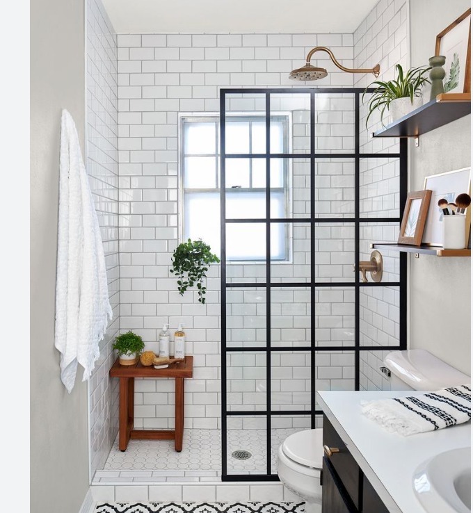 Nowoczesna łazienka z kabiną prysznicową typu walk-in z czarnymi ramami, białe płytki metra na ścianach, drewniany stołek z kosmetykami i wzorzysta podłoga w strefie wejścia.