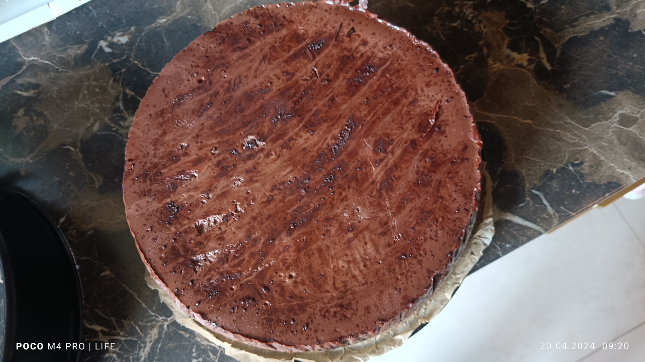 Czekoladowy tort na papierze do pieczenia, widoczny z góry, z marmurkowym blatem w tle.