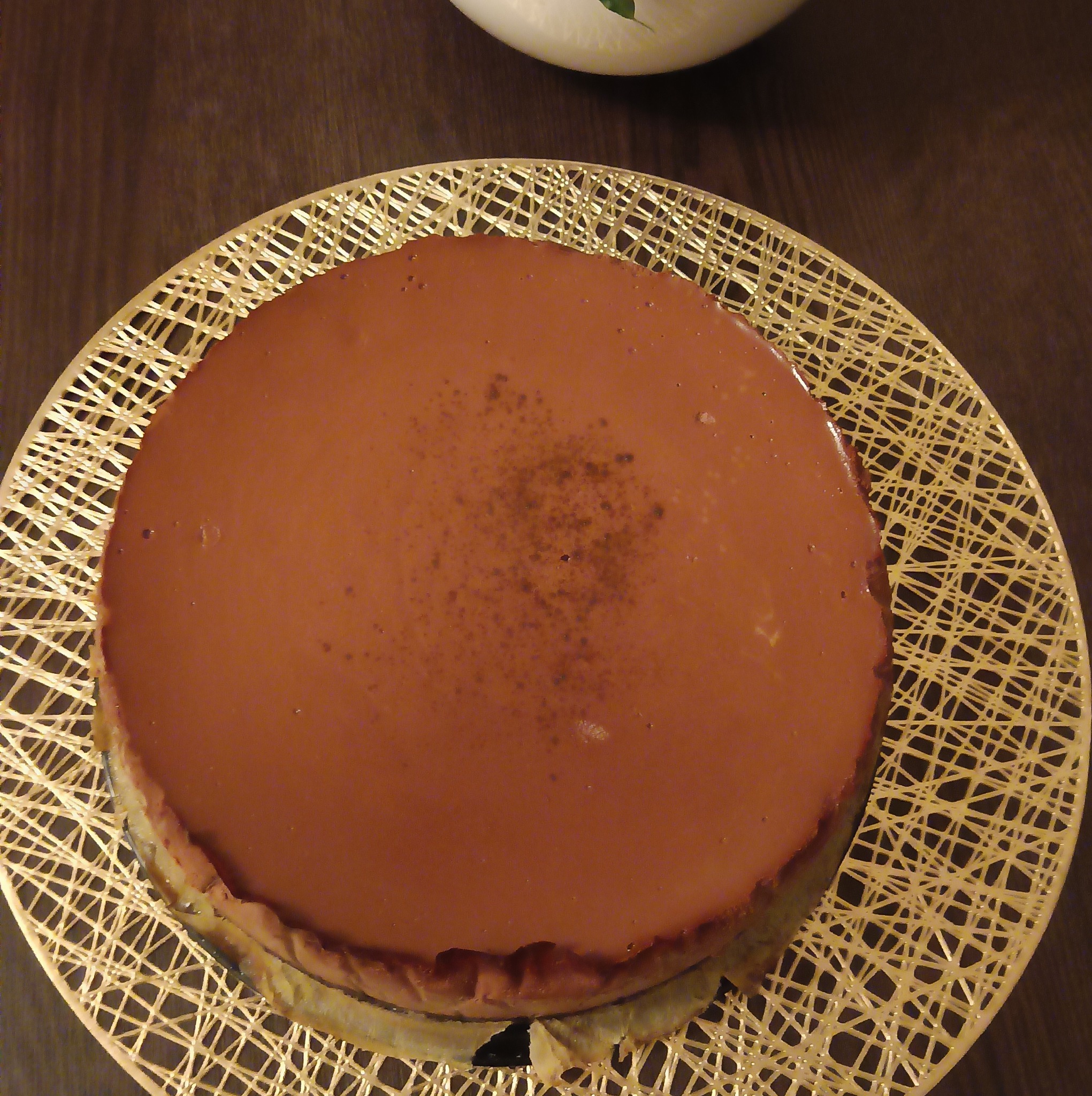 Czekoladowy tort na złotym ażurowym podkładzie, widoczny z góry, z delikatnym posypem na środku.