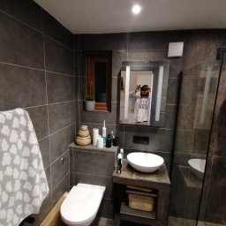 Łukasz szydlik - Nowoczesna łazienka z ciemnymi, grafitowymi płytkami, kabiną prysznicową typu walk-in, wiszącą miską WC i umywalką nablatową. W lustrze odbija się osoba robiąca zdjęcie.