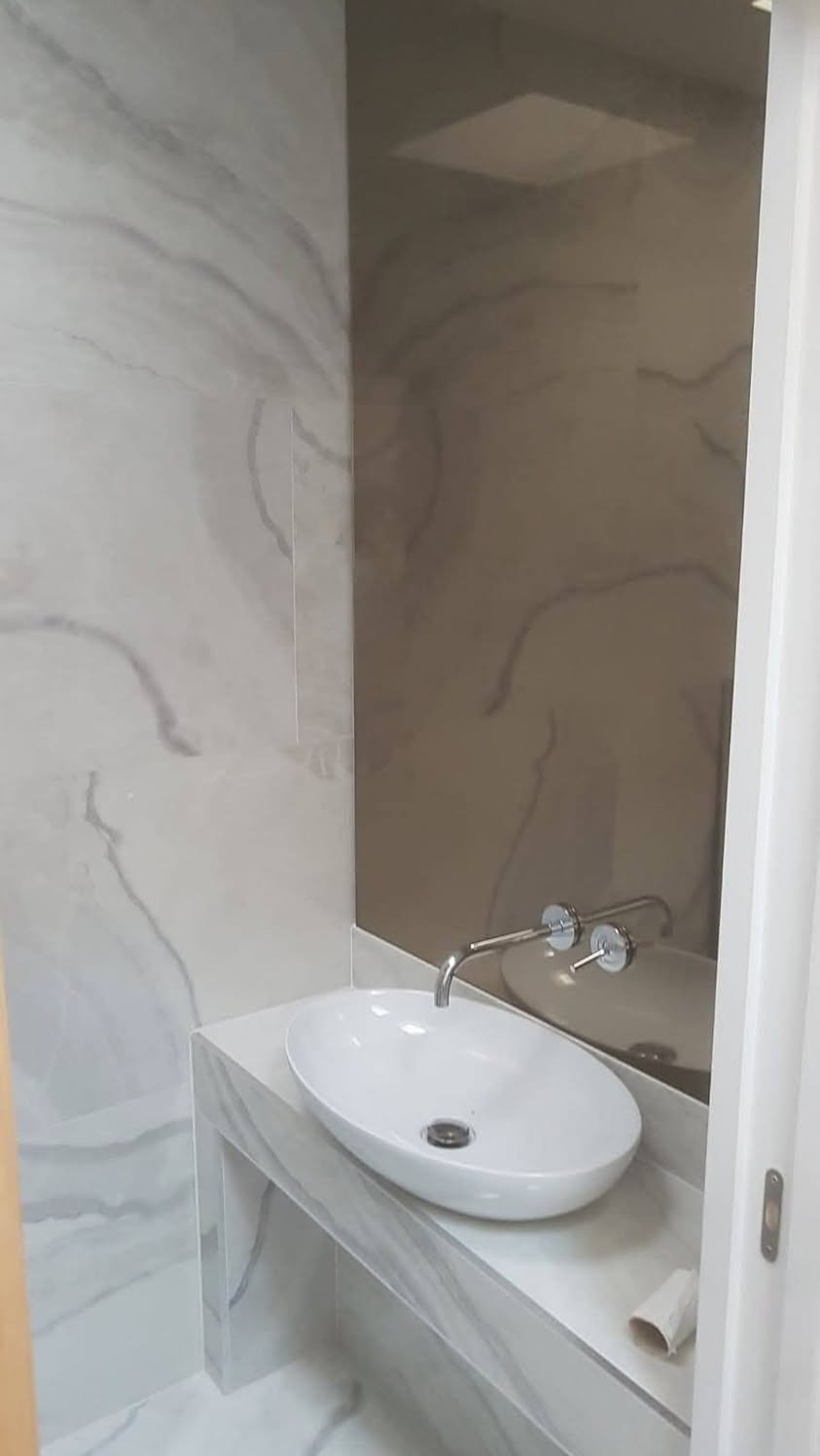 Nowoczesna łazienka z owalną umywalką nablatową, chromowaną armaturą i okładziną ścienną z marmuru w odcieniach szarości, uzupełniona lustrem w kolorze przydymionego brązu.