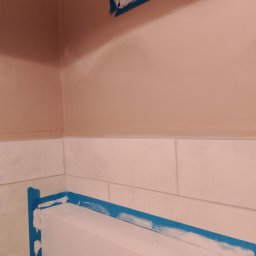 Krzysztof Ścibura - Ściana i listwa przypodłogowa zabezpieczone taśmą malarską, fragment okna w górnym rogu, ślady świeżego malowania.