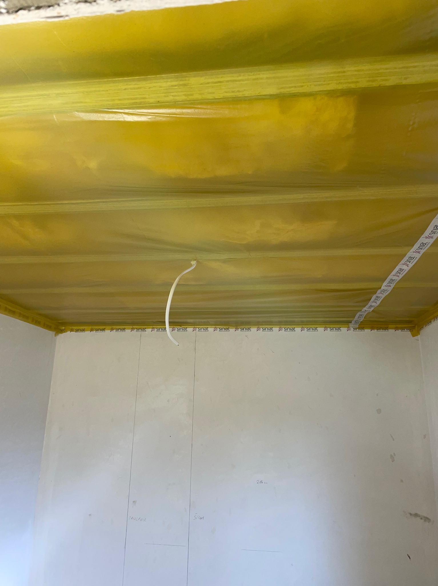 Przygotowanie do malowania: Sufit i ściany zabezpieczone folią malarską i taśmą marki Siniat, widoczne oznaczenia ołówkiem na ścianie.