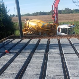 Mirosław Janowski. - Wylewka stropu Teriva z betoniarki na budowie w Wieleniu, widoczne bloczki betonowe, stalowe pręty zbrojeniowe i rura do podawania betonu.