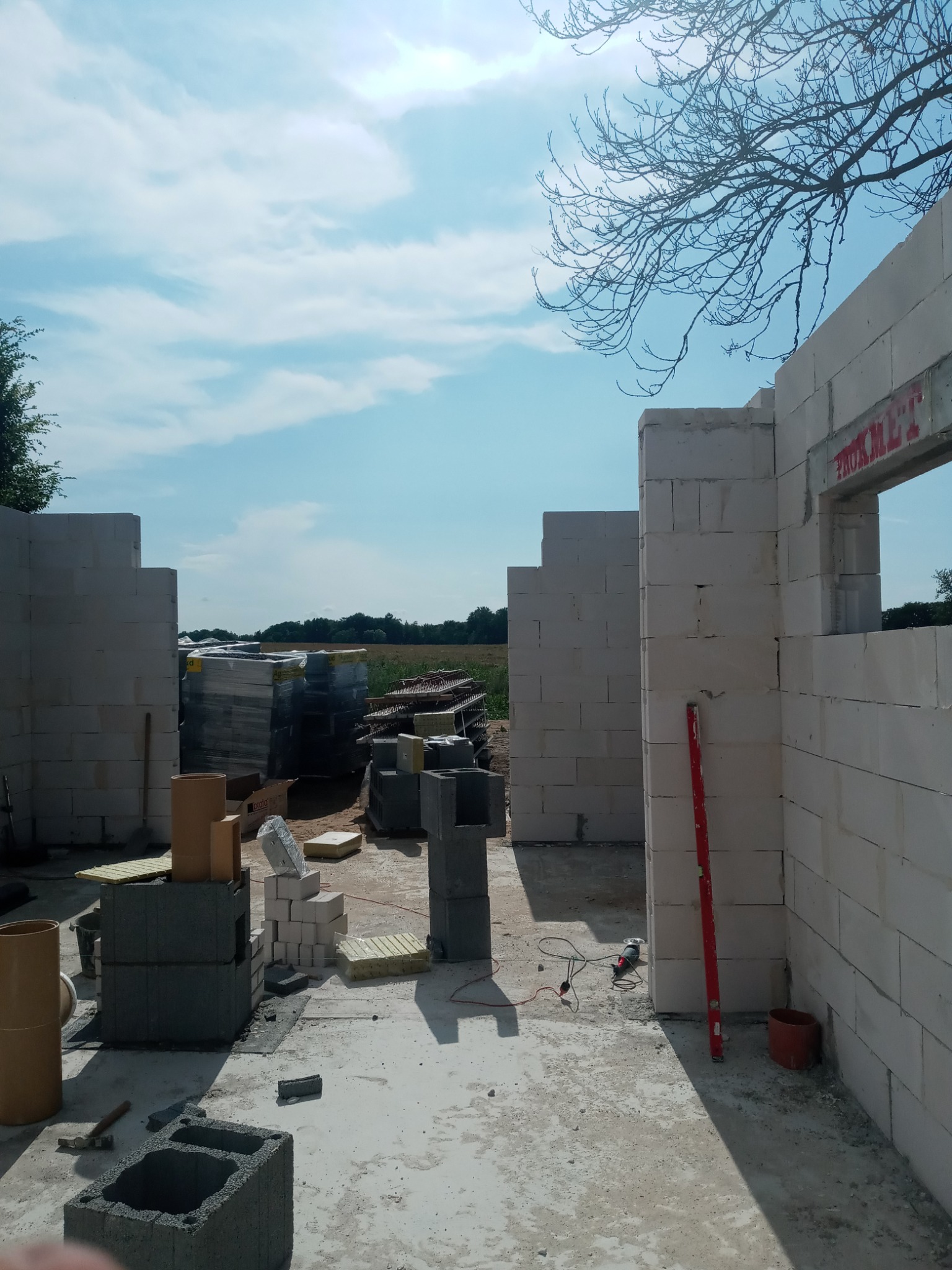 Wznoszenie ścian budynku z betonu komórkowego, widoczny poziomica, szlifierka kątowa i paleta z materiałem budowlanym w tle.